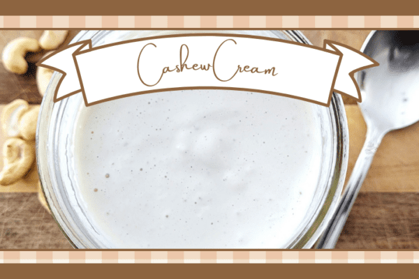 Jar of cashew cream on a wooden board with whole cashews scattered around it