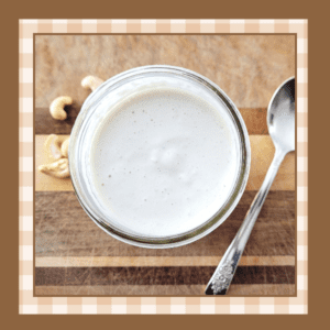 Jar of cashew cream on a wooden board with whole cashews scattered around it