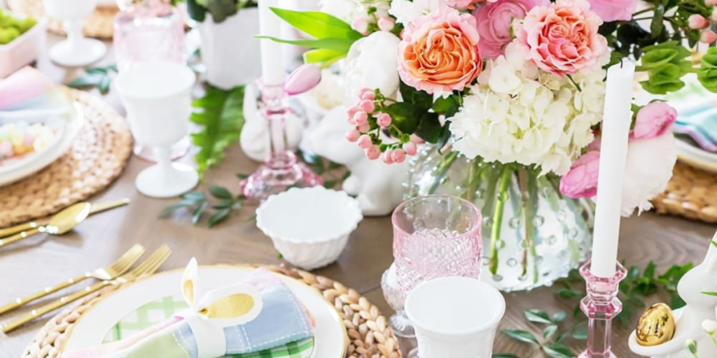 Easter table set with hyacinth chargers, pastel plaid napkins, milk glass goblets. The centerpiece includes a hobnail vase filled with pastel flowers, flanked by pink candlesticks and white ceramic bunnies.