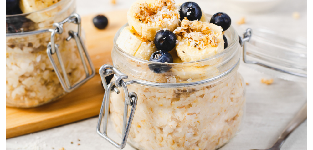 Closeup of short canning jar with overnight oats topped with sliced bananas, blueberries, and chopped nuts.