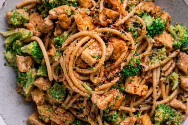 Tofu Noodle Bowl | The Granite Acorn Closeup of serving bowl with whole wheat noodles broccoli and tofu chunks in an almond butter sauce
