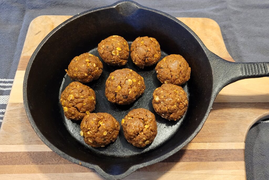 Cast iron skillet with vegan meatballs on a wooden cutting board