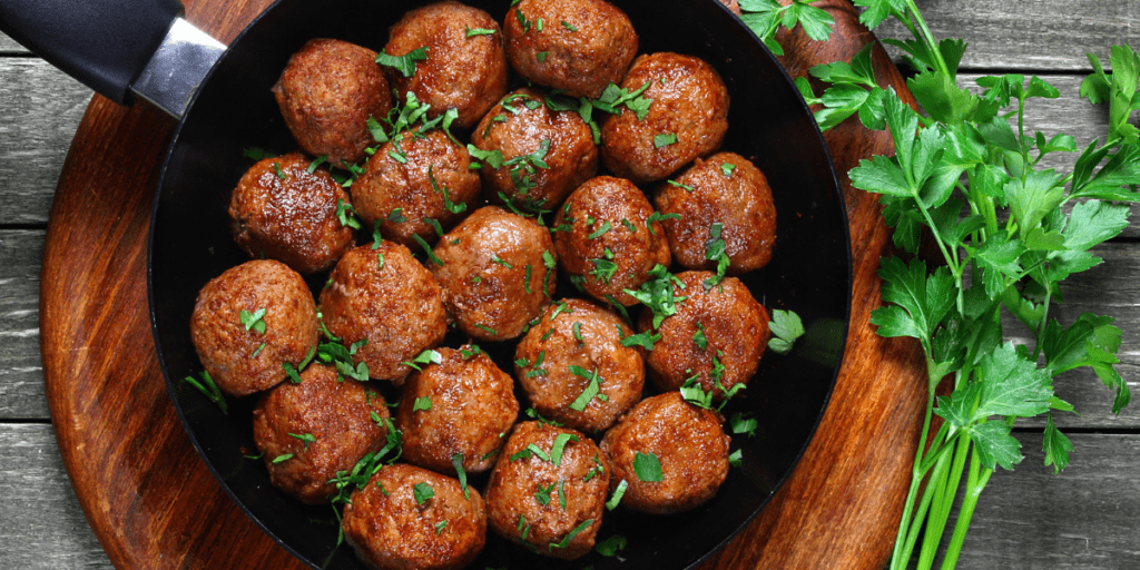 Skillet filled with vegan meatballs sprinkled with chopped parsley on a wooden cutting board. Sprigs of fresh parsley are laid to the side of the skillet.