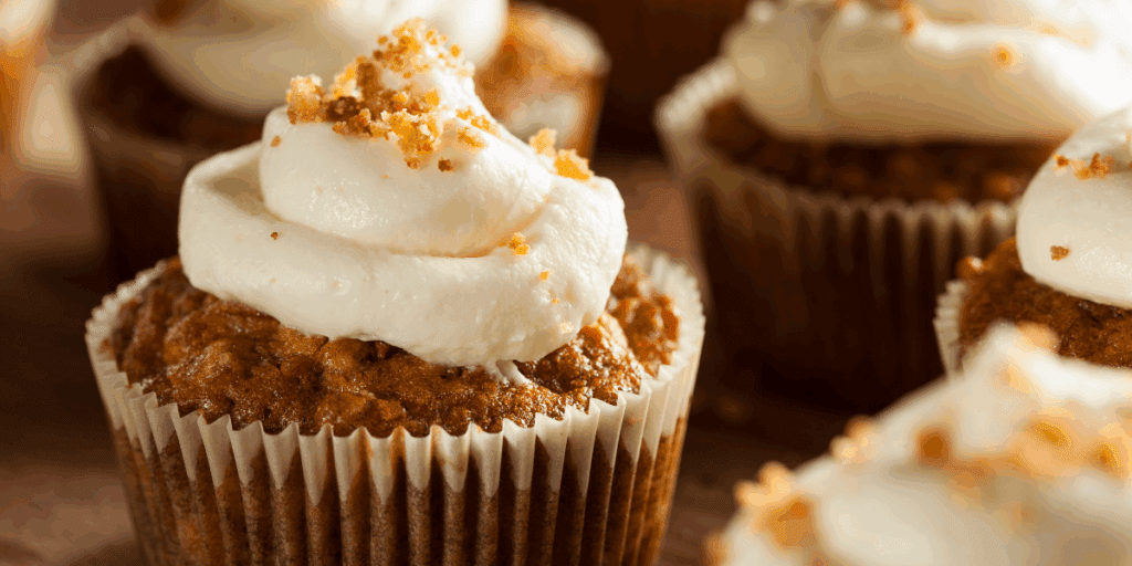 Closeup of a carrot cake cupcake with cream cheese frosting and a sprinkle of chopped nuts on top.