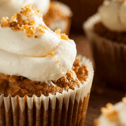 Closeup of a carrot cake cupcake with cream cheese frosting and a sprinkle of chopped nuts on top.