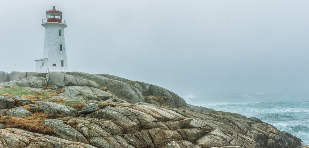 Image of rocky shore and lighthouse on the coast shrouded in fog