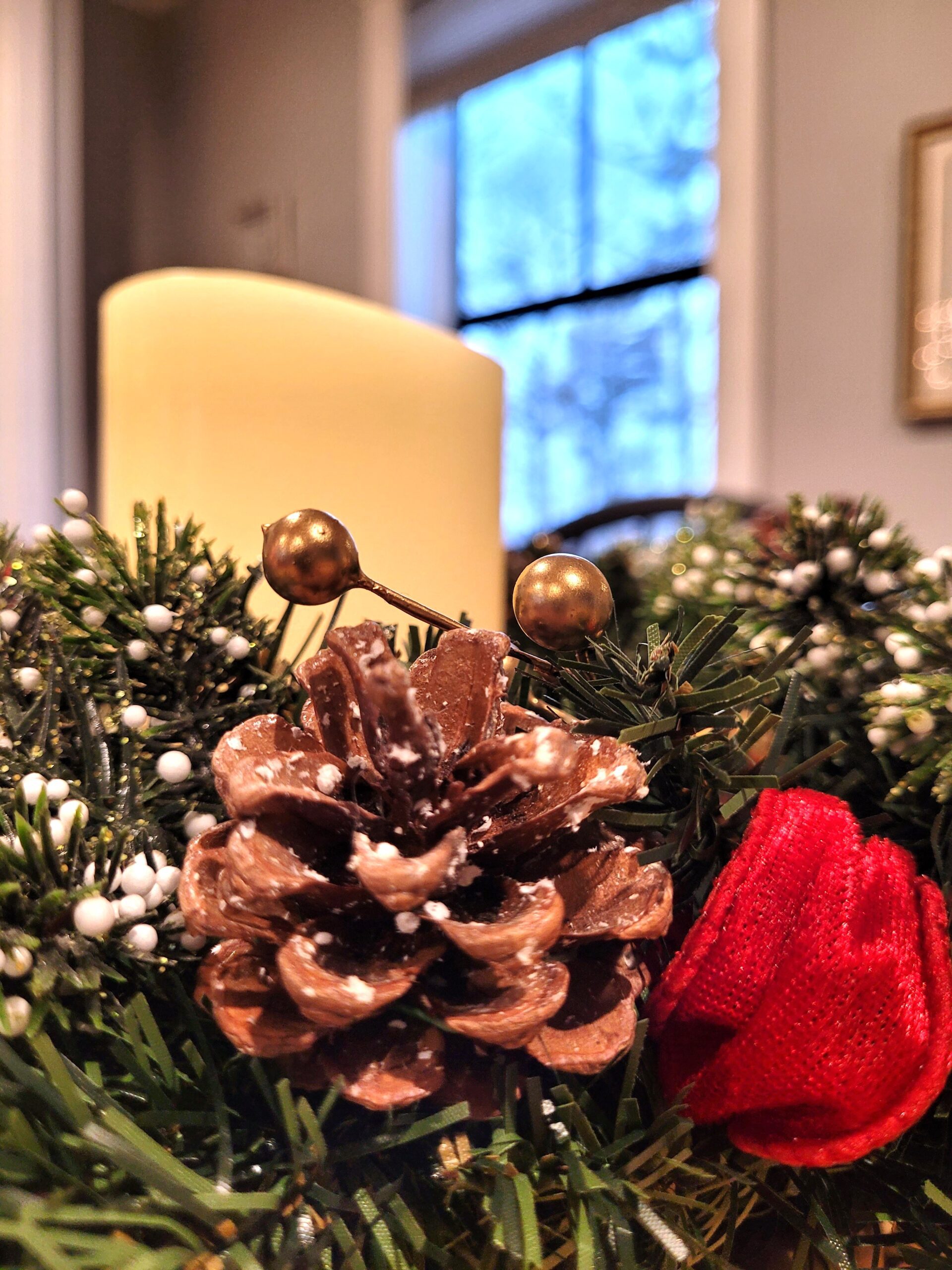 Closeup of holiday wreath candle ring featuring a pine cone red velvet ribbon gold berries and snowy evergreen picks