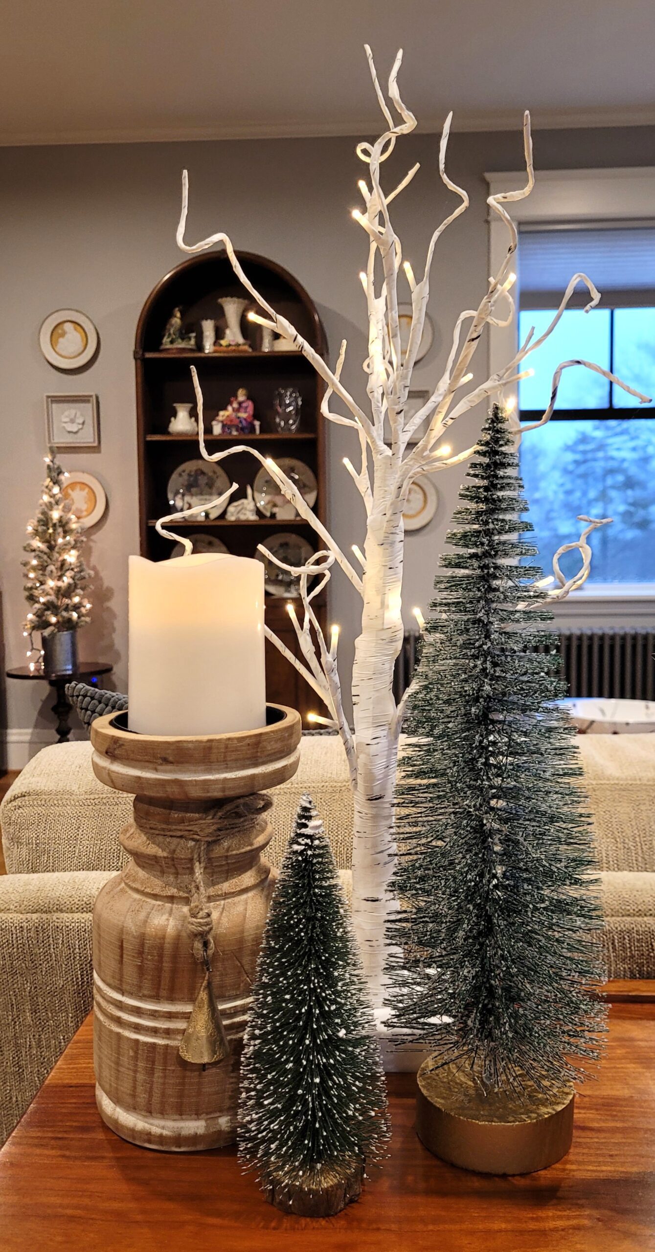 Closeup of pillar candles in wood holders bottle brush trees and faux birch trees