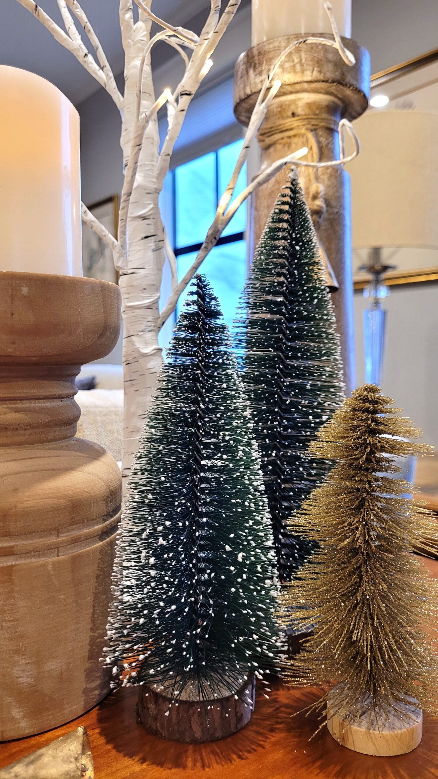 Closeup of pillar candles in wood holders bottle brush trees and faux birch trees