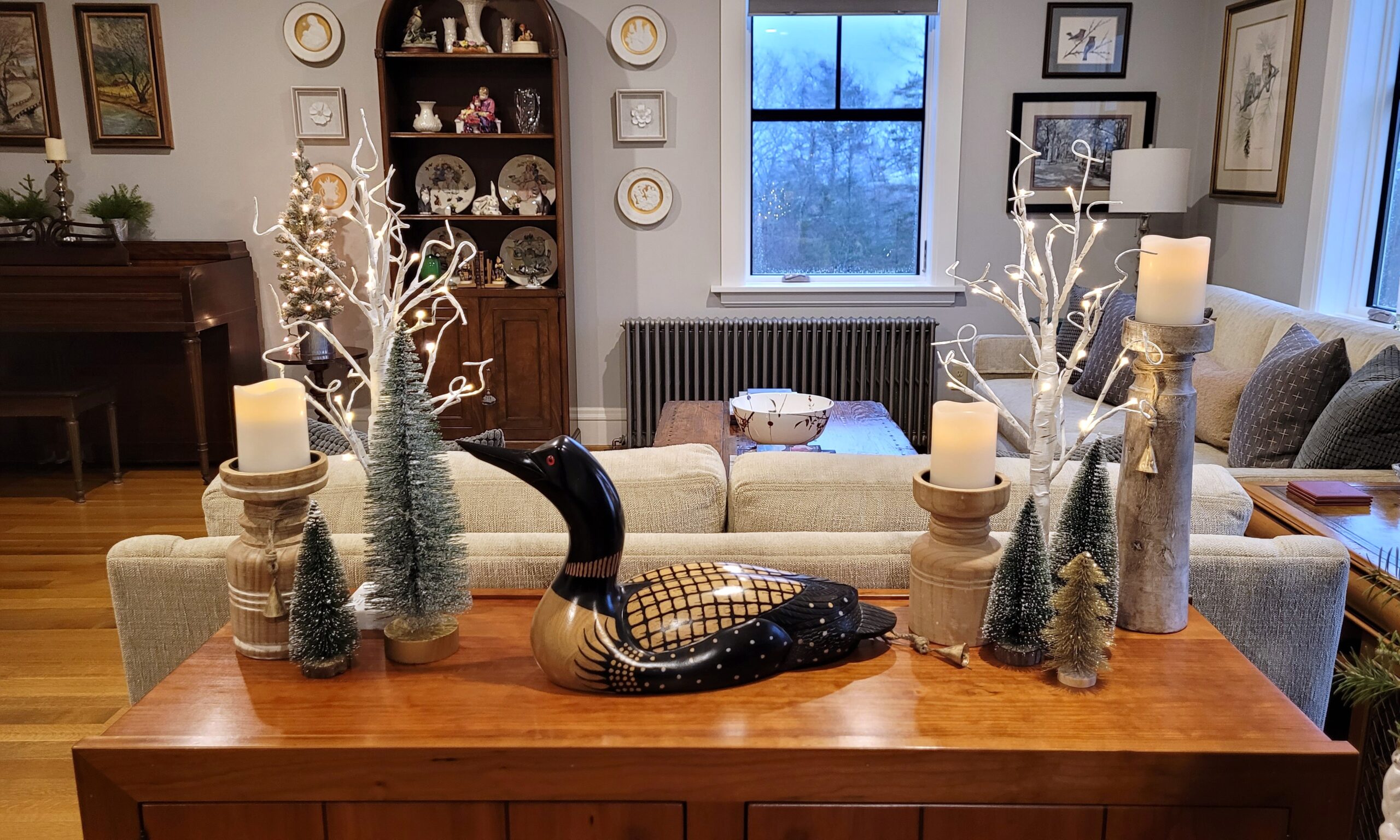Wood credenza with a carved loon pillar candles in wood holders bottle brush trees and faux birch trees