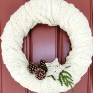 Ivory cable knit scarf wreath with pine cones, a yarn star, and greenery
