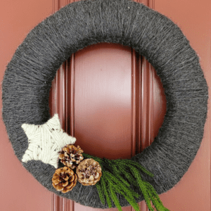 Gray yarn wreath with yarn star, pinecones, and greenery
