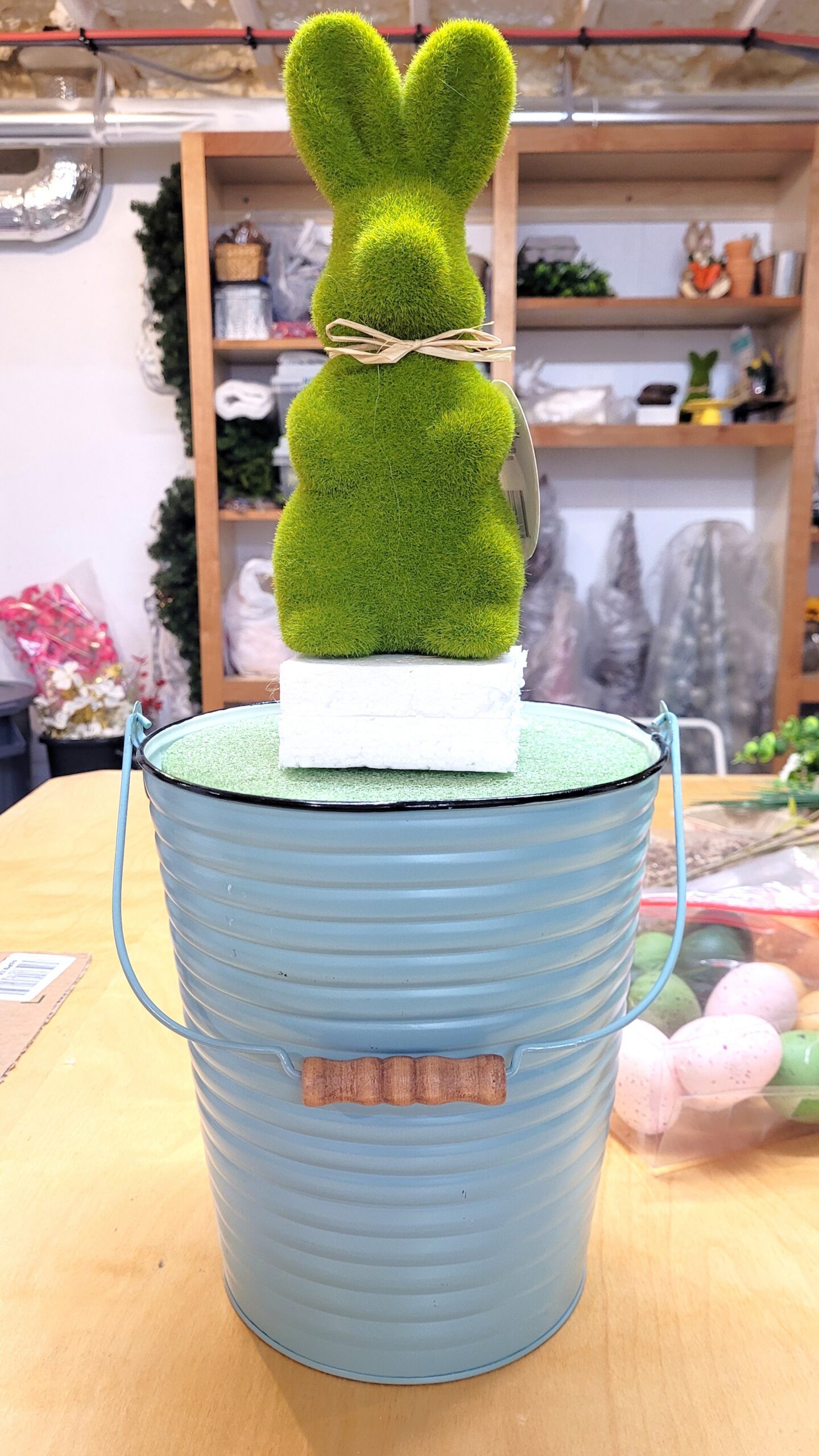 Green moss bunny centerpiece being made The bunny is attached to foam blocks in a pastel blue pail