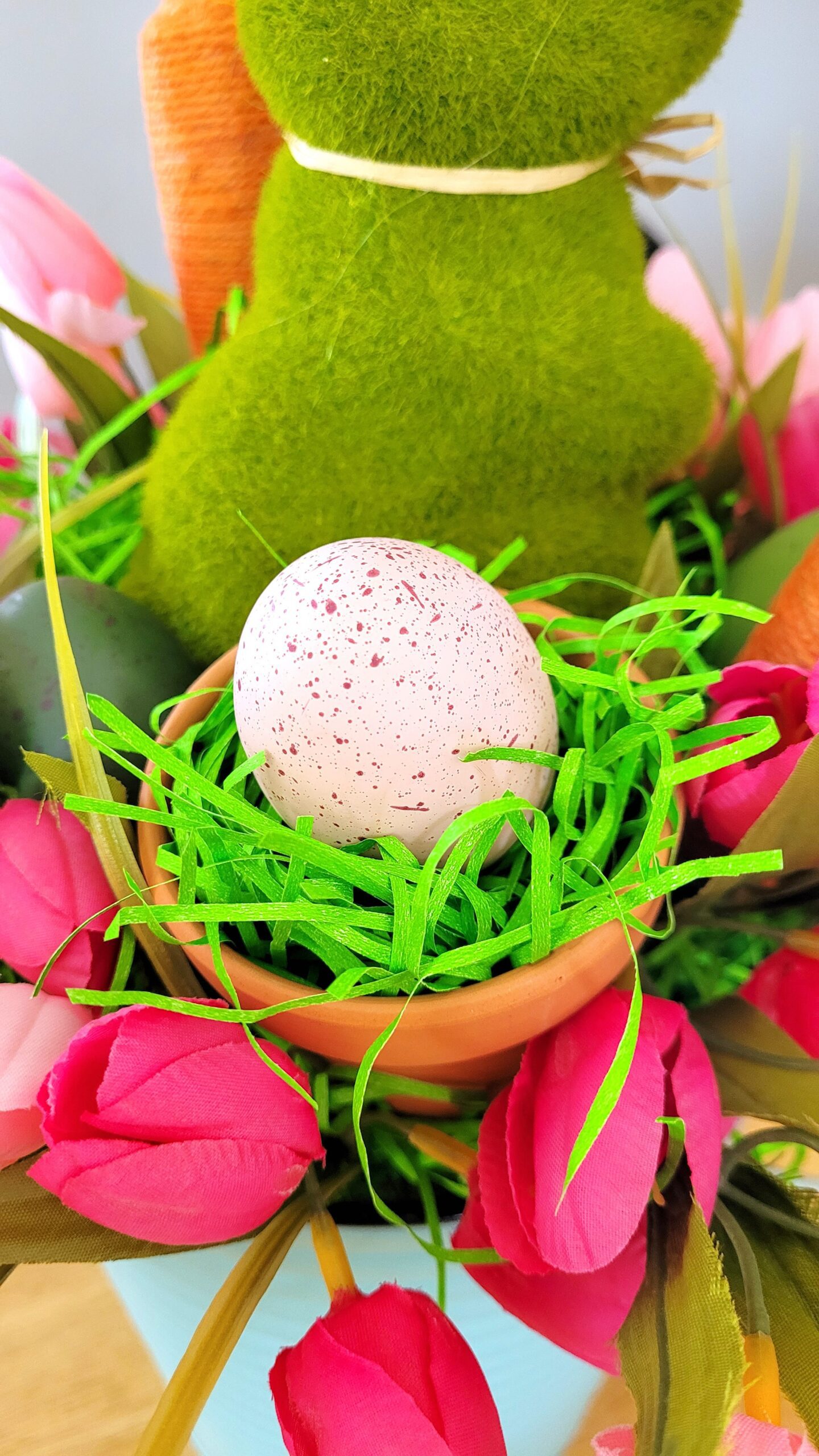 Closeup of a faux pink speckled easter egg in a mini terracotta pot with green easter grass