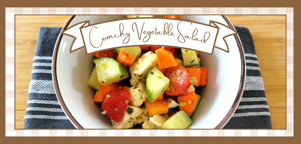 Bowl of crunchy vegetable salad with diced carrots, cucumbers, tomatoes and cauliflower on a striped napkin; a banner above reads 'Crunchy Vegetable Salad'.