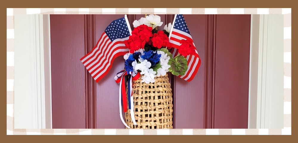 Memorial-Day-Banner | The Granite Acorn Basket filled with white and blue hydrangea and red geraniums Two small american flags are tucked in and red white and blue ribbons are tied on the side It hangs on a red front door