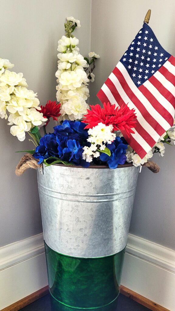 Memorial-Day-Kitchen-Porch-2 | The Granite Acorn Green and silver galvanized bucket holding faux ivory lilac stems blue hydrangea and red daisies with an american flag tucked in