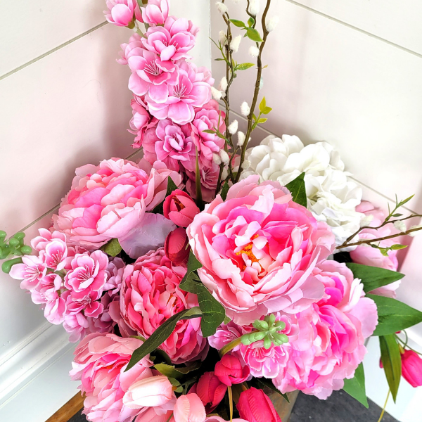 Bouquet of pink peonies with white hydrangeas and pussy willow branches in a corner against tiled walls