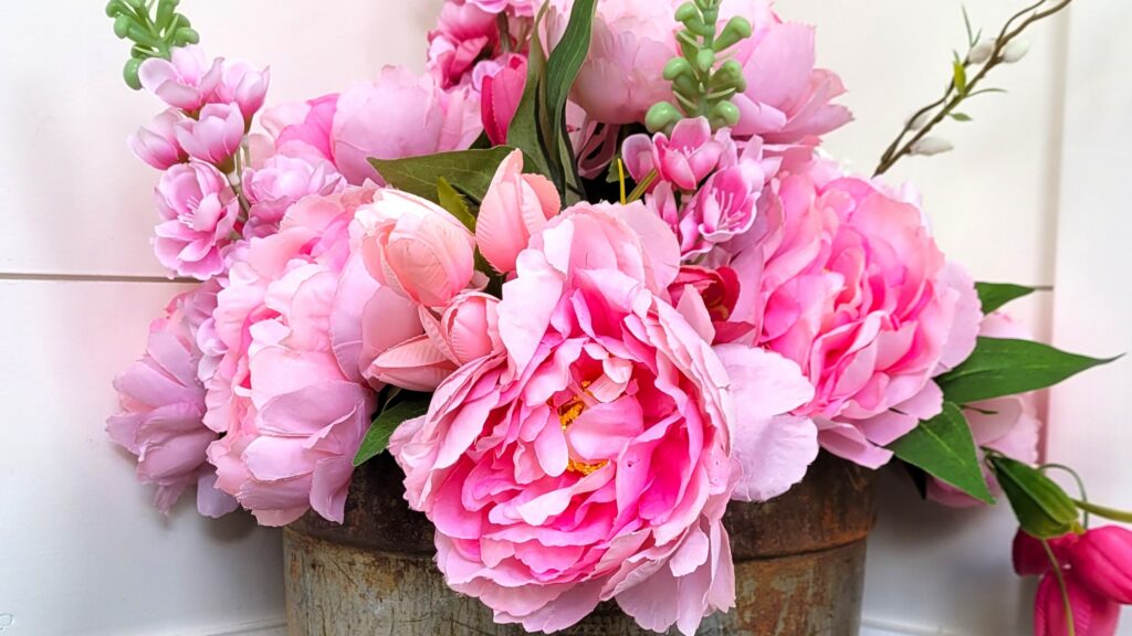 Bunch of pink peonies snapdragons tulips and a white hydrangea blossom It's in a weathered sap bucket.