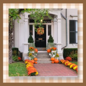 White front porch decorated for fall with pumpkins and orange mums along brick walkway.